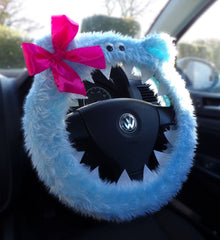 Blue fuzzy steering wheel cover with a pink bow on a Volkswagen steering wheel.
